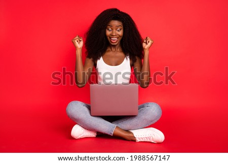 Full body photo of young attractive afro girl happy positive smile look laptop rejoice victory isolated over red color background