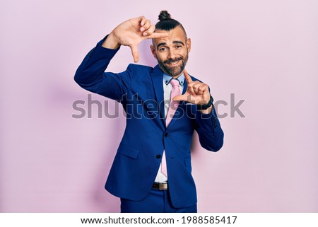 Young hispanic man wearing business suit and tie smiling making frame with hands and fingers with happy face. creativity and photography concept. 