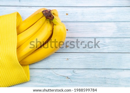 yellow bananas lying in a yellow bag on a blue wooden background.