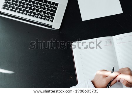 Photo from above. Female hands hold a pen while signing documents next to a laptop. Office work concept