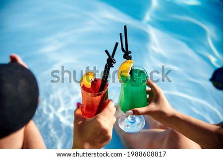 two cocktails in women's hands on the background of water