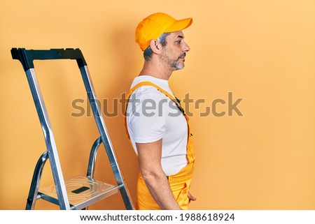 Handsome middle age man with grey hair holding ladder looking to side, relax profile pose with natural face with confident smile. 