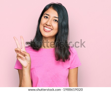 Beautiful asian young woman wearing casual pink t shirt showing and pointing up with fingers number two while smiling confident and happy. 