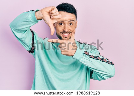Young hispanic man wearing casual clothes smiling making frame with hands and fingers with happy face. creativity and photography concept. 