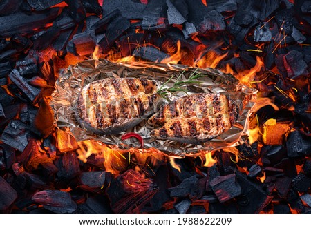Roasted salmon steaks in aluminum foil on bbq grate over hot pieces of coals. Top view.