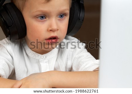 Blue-eyed boy watches and listens using a laptop at home, using an online app, social distancing, home schooling, distance learning during the covid-19 coronavirus pandemic.