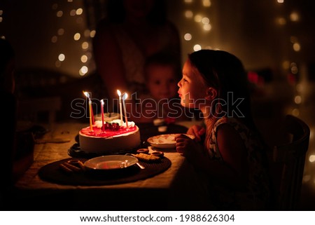 birthday cake on children's day of birth, child girl blows out the candles on the cake, soft focus and dark style, lifestyle