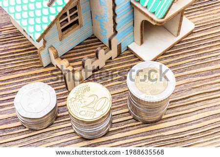 The concept of mortgage, sale and rental of housing and real estate. Buying a home. A mock house with stacks of coins in the foreground on a wooden surface. Banner format. Copy space