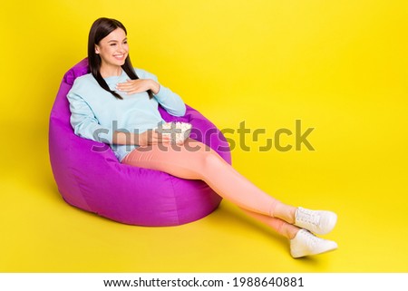 Full length body size photo girl laying in beanbag watching movie eating pop corn isolated vibrant yellow color background