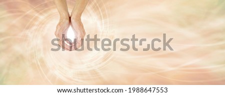 Healer sending Unconditional Love Healing Energy -  female cupped hands making an O shape with a bright light between against a pale golden vortex energy field flowing across and space for messages
 Royalty-Free Stock Photo #1988647553