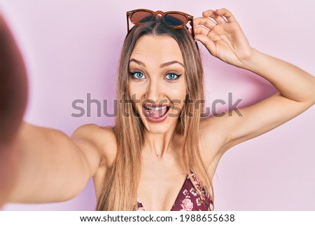Young blonde girl wearing bikini taking a selfie celebrating crazy and amazed for success with open eyes screaming excited. 