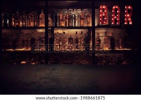 Vintage BAR sign with lights in the dark with bottles of alcohol and empty tabletop. 