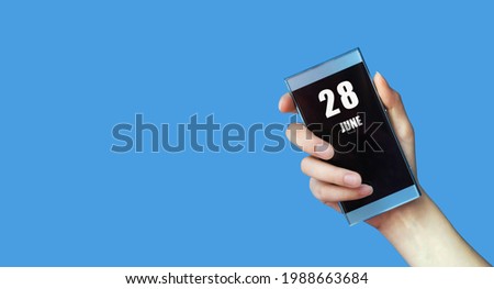 june 28. 28th day of the month, calendar date.Woman's hand holds mobile phone with blank screen on blue isolated background. Summer month, day of the year concept.