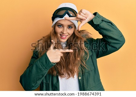 Beautiful blonde caucasian woman wearing snow wear and sky glasses smiling making frame with hands and fingers with happy face. creativity and photography concept. 