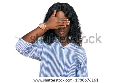 Beautiful african young woman wearing casual clothes and glasses covering eyes with hand, looking serious and sad. sightless, hiding and rejection concept 