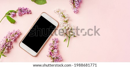 A smartphone with a blank screen lies in the middle of a floral composition of lilac. Flat lay, top view mockup copy space.