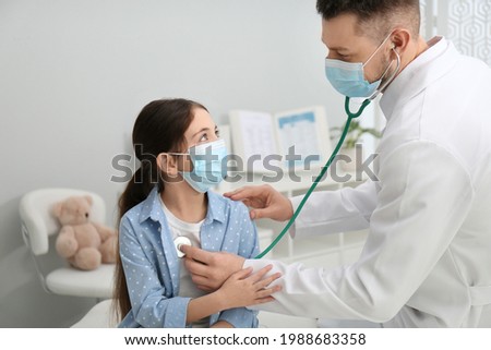 Pediatrician examining little girl in hospital. Doctor and patient wearing protective masks Royalty-Free Stock Photo #1988683358