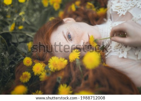 Portrait of a red-haired woman among yellow dandelions