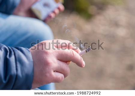 closeup person's hand hold incense a cigarette next carton cigarettes pack box.Outdoor shot.