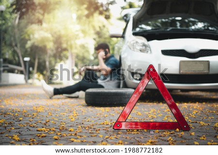 Asian man sitting beside car and using mobile phone calling for assistance after a car breakdown on street. Concept of vehicle engine problem or accident and emergency help from Professional mechanic Royalty-Free Stock Photo #1988772182