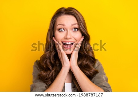 Photo of impressed pretty young lady wear green shirt arms cheeks open mouth smiling isolated yellow color background
