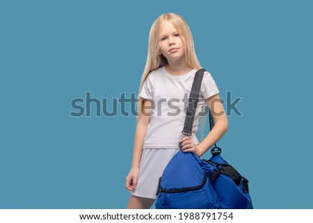 Girl with sports bag standing on blue background