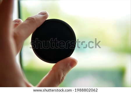 the person holds the nd1000 gray filter in their fingers. Neutral gray filter used in photography to extend the shutter speed