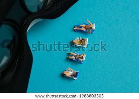 Miniature people toy figure photography. Virtual travel concept, group of men and girl relaxing seat while watching in front of goggles device, isolated on blue background. Image photo