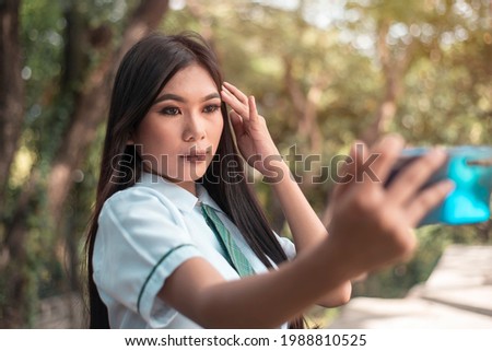 A pretty vain young asian woman in a student uniform takes a selfie of herself while outdoors. Taking a photo for social media.