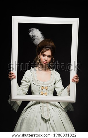 charming woman in elegant vintage outfit holding white framing isolated on black