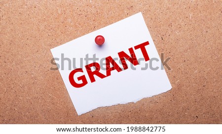 White paper with the text GRANT is attached to the wooden background with a red button.