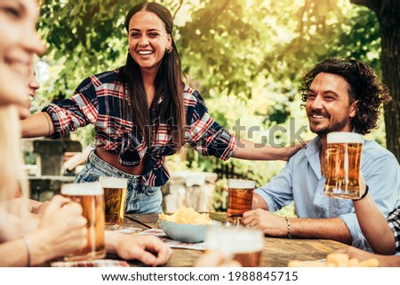 Happy friends celebrating drinking beer pint at park outdoor - Young people talking and laughing together at brewery pub garden - Friendship, youth and beverage concept Royalty-Free Stock Photo #1988845715