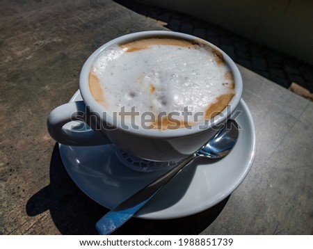 View of a white breakfast cappuccino coffee on the dark table in an outdoor terrace in the summer in bright sunlight