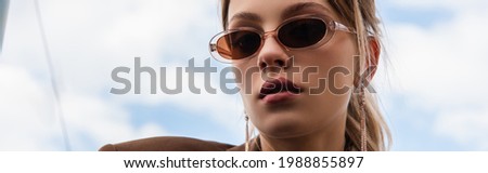 young woman in sunglasses posing against blue sky, banner