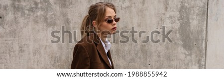 dreamy young model in stylish sunglasses and trendy suit posing on rooftop, banner