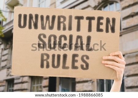 The phrase " Unwritten social rules " on a banner in men's hand. Human holds a cardboard with an inscription. Friendship. Communication. Communicate. Relationship. Social issues
