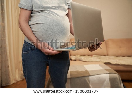 Pregnant woman at home is standing with laptop, concept: online shopping or home office. High quality photo