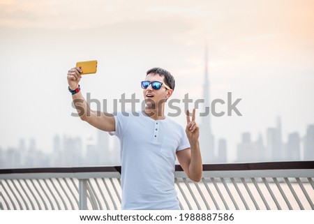 A male traveler takes a selfie on his smartphone against the backdrop of the skyscrapers of Dubai and the Creek Channel Bay