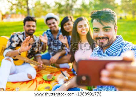 indian students having a lunch and taking selfie on camera phone in Delhi park outdoors