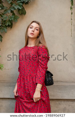 A girl in a red floral dress on a background of a beige wall. Vertical Portrait of a beautiful gir