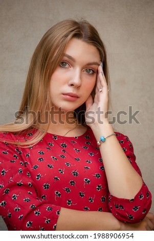 A girl in a red floral dress on a background of a beige wall. Vertical Portrait of a beautiful gir