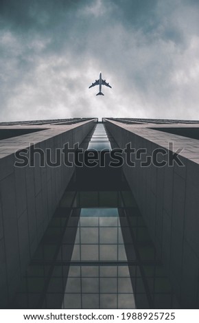 Low angle view of modern tall business building. Commercial jet plane flying over skyscraper. Against dramatic cloudy sky before storm.