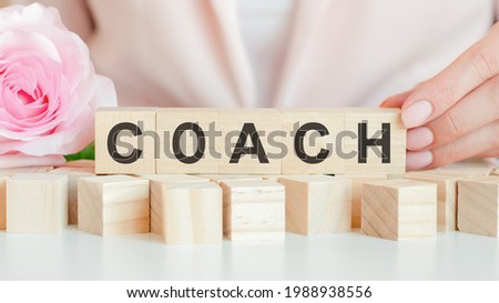 woman holds a wooden cube with the text of coach in her hand. on the wooden cubes there is a living rose flower. pink background, front view. business, economic, education concept