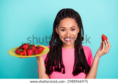Photo of joyful braids hairstyle young lady hold strawberries wear pink t-shirt isolated on teal color background