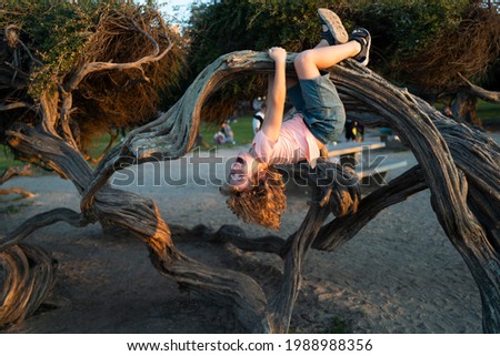 Kid climbing tree. Caucasian boy happily lying upside down in a tree hugging a big branch. Royalty-Free Stock Photo #1988988356