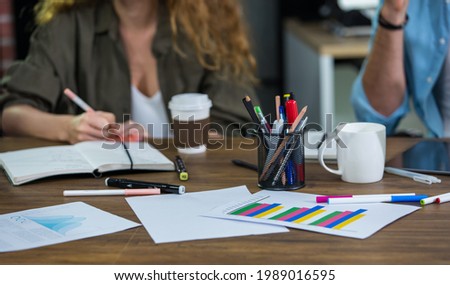 Selective focus office supplies consists of pencils, paper of financial or marketing graph information report on table with blur background of colleagues brainstorming ideas in modern meeting room Royalty-Free Stock Photo #1989016595