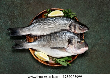 Uncooked fish with lime and herbs in a wooden bowl on a dark green background top view. Raw dorada and seabass. Royalty-Free Stock Photo #1989026099