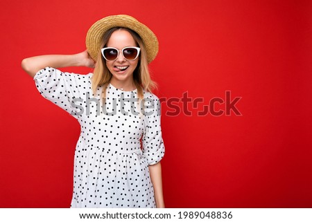 Photo shot of beautiful positive young blonde woman wearing summer casual clothes and stylish sunglasses isolated over colorful background looking at camera