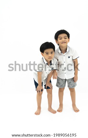 Picture of twin asian boys standing together with funny face on white background. Looking at camera.