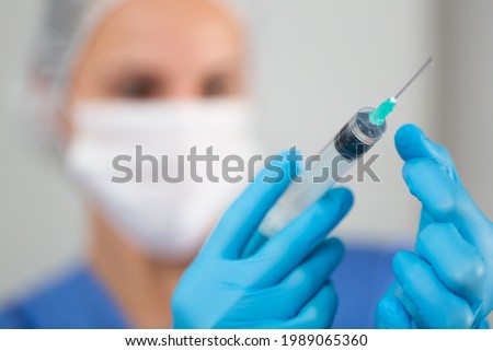 Experienced masked nurse working in the treatment room prepared a syringe for injection, filling it with medicine